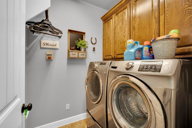 Clothes washing area featuring light tile patterned floors, cabinets, and washer and dryer | Image 25