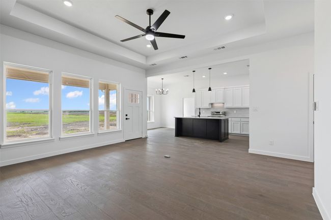 Unfurnished living room with a raised ceiling, ceiling fan with notable chandelier, recessed lighting, and visible vents | Image 9