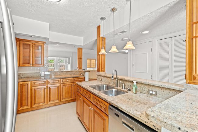 Kitchen with dishwasher, a textured ceiling, light stone counters, brown cabinetry, and hanging light fixtures | Image 9