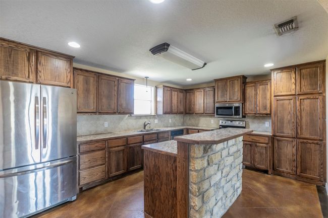 Kitchen featuring stainless steel appliances, a kitchen island, a sink, visible vents, and decorative backsplash | Image 6