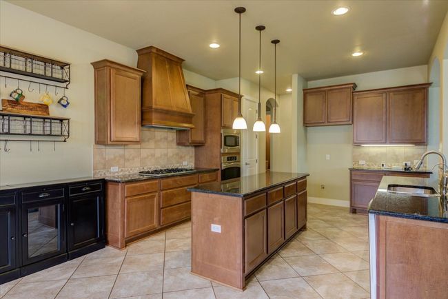 Kitchen featuring custom range hood, a sink, appliances with stainless steel finishes, and wood cabinetry | Image 13