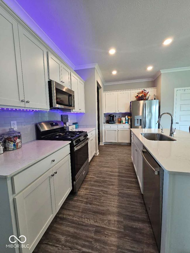 kitchen with stainless steel appliances, a sink, ornamental molding, light countertops, and backsplash | Image 6