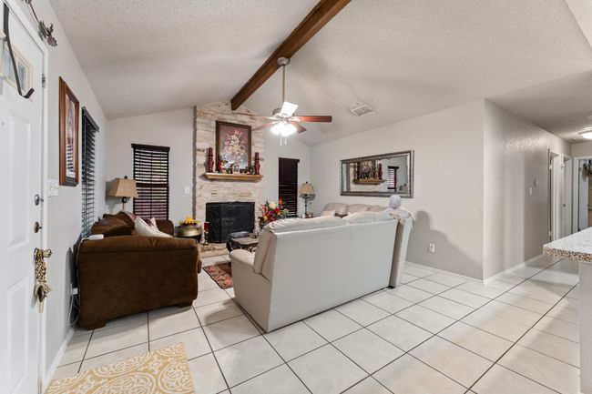Living area featuring a textured ceiling, light tile patterned floors, a ceiling fan, and a stone fireplace | Image 5