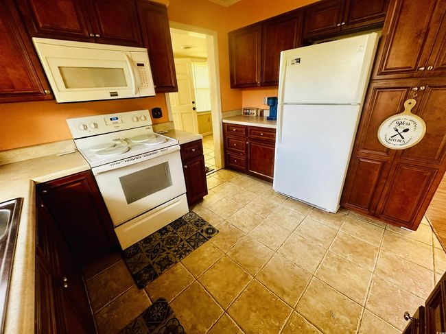 Kitchen with light tile patterned floors, light countertops, white appliances, and reddish brown cabinets | Image 8