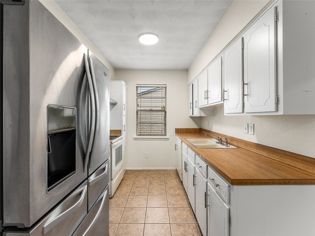 Kitchen featuring white cabinetry, sink, light tile patterned floors, electric range, and stainless steel refrigerator with ice dispenser | Image 11
