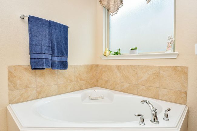 Bathroom features a corner bathtub with chrome fixtures, surrounded by beige tiled walls. | Image 21