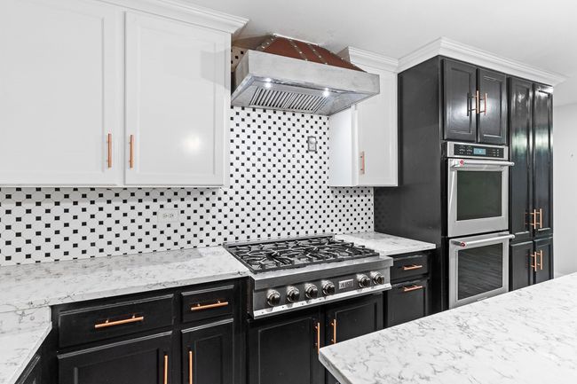 Kitchen featuring appliances with stainless steel finishes, custom range hood, decorative backsplash, dark cabinets, and white cabinetry | Image 21