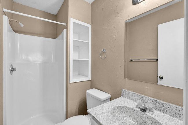 Bathroom with a shower stall, toilet, vanity, and a textured wall | Image 15