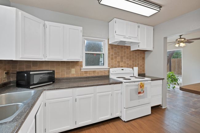Kitchen featuring black microwave, dark countertops, white electric range oven, under cabinet range hood, and white cabinetry | Image 15