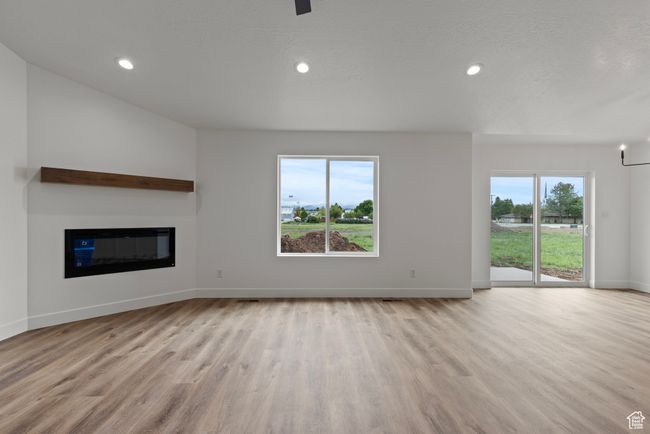 Unfurnished living room with wood finished floors, baseboards, a glass covered fireplace, and recessed lighting | Image 4