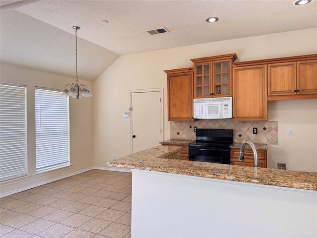 Kitchen with white microwave, black electric range, brown cabinets, backsplash, and vaulted ceiling | Image 7