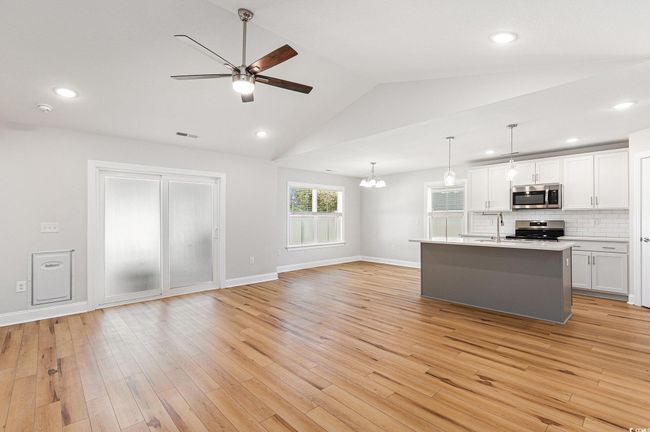 Kitchen with appliances with stainless steel finishes, a ceiling fan, open floor plan, white cabinets, and lofted ceiling | Image 7