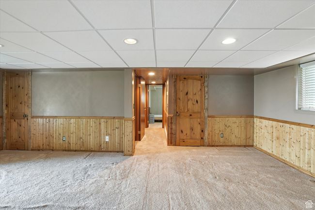 Basement living room with a paneled ceiling, a wainscoted wall, carpet flooring, wooden walls, and recessed lighting | Image 20