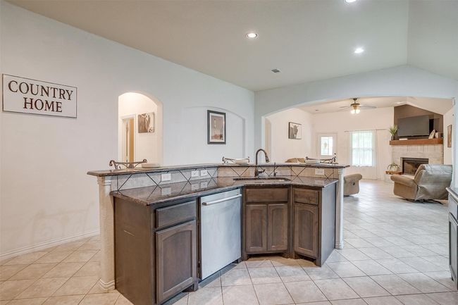 Kitchen featuring stainless steel dishwasher, arched walkways, a ceiling fan, a fireplace with raised hearth, and vaulted ceiling | Image 14