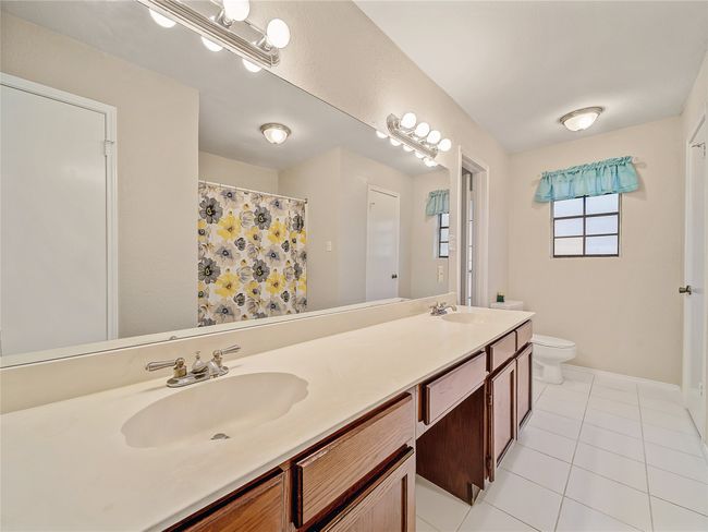 Full bathroom with toilet, tile patterned floors, double vanity, baseboards, and curtained shower | Image 16