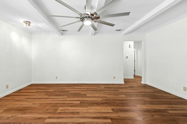 Unfurnished room featuring beamed ceiling, ceiling fan, wood finished floors, and crown molding | Image 15