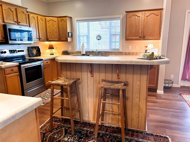 Kitchen featuring dark wood-style floors, a breakfast bar area, light countertops, and appliances with stainless steel finishes | Image 15