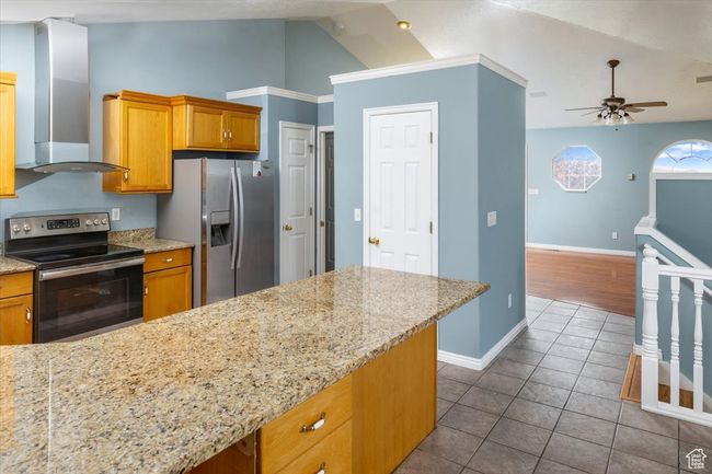 Kitchen with appliances with stainless steel finishes, light stone counters, wall chimney exhaust hood, lofted ceiling, and ceiling fan | Image 15