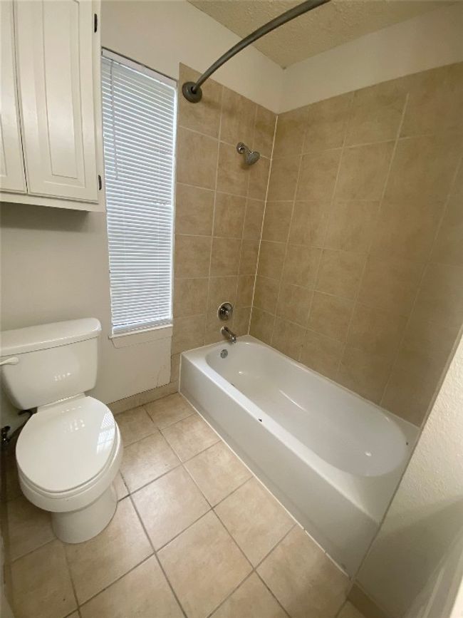 Bathroom featuring shower / tub combination, toilet, a textured ceiling, baseboards, and tile patterned flooring | Image 10