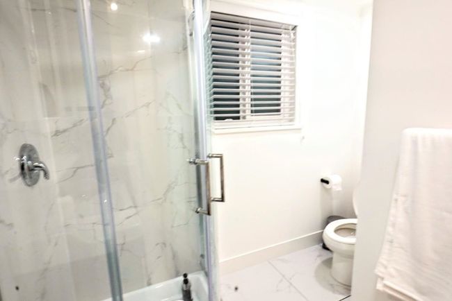 Full bathroom featuring marble look tile flooring, toilet, a marble finish shower, and baseboards | Image 35