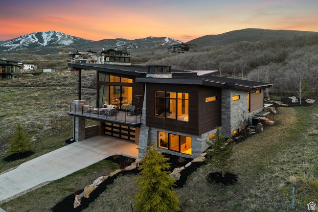 Back of property at dusk with a mountain view, driveway, a garage, a balcony, and a yard | Image 10