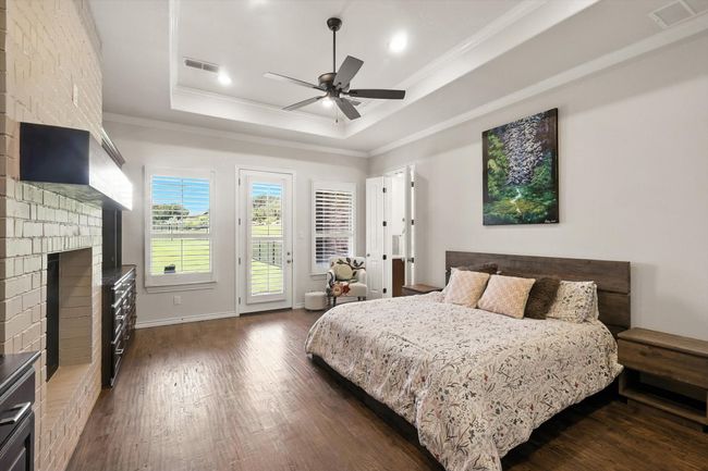 Bedroom with ornamental molding, access to outside, a tray ceiling, dark wood-style floors, and a fireplace | Image 19
