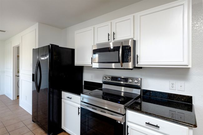 Kitchen featuring white cabinets, light tile patterned floors, and stainless steel appliances | Image 12