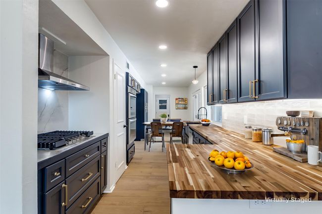 Kitchen with wooden counters, exhaust hood, appliances with stainless steel finishes, backsplash, and light wood-style floors | Image 10
