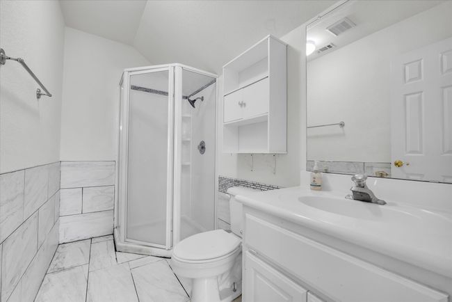 Full bath featuring a stall shower, vanity, toilet, marble look tiles, and tile walls | Image 24