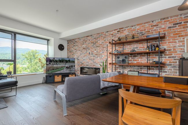 Living area with wood finished floors, a fireplace, and brick wall | Image 9