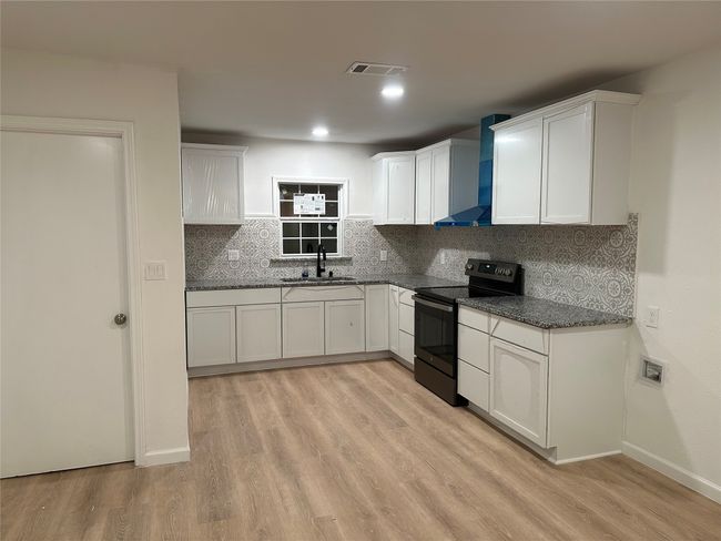 Kitchen with white cabinets, stainless steel electric range, a sink, and wall chimney exhaust hood | Image 4
