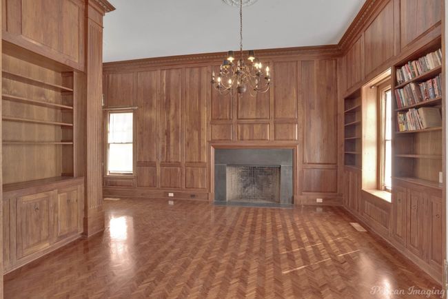 Unfurnished living room featuring built in shelves, wooden walls, a chandelier, and a fireplace | Image 16
