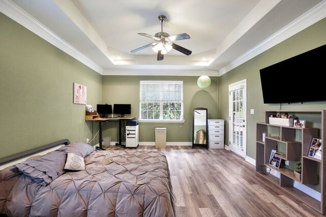 Bedroom with a raised ceiling, wood finished floors, ornamental molding, an office area, and a ceiling fan | Image 18