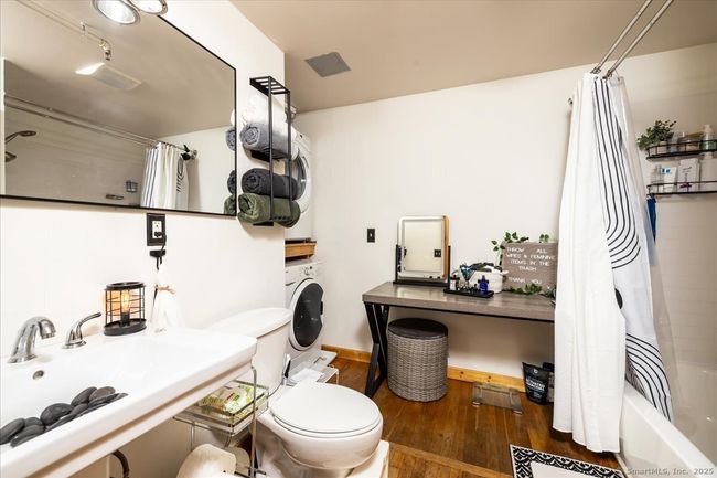 well-lit bathroom with a clean, modern design, featuring a white pedestal sink, tub and shower condo, Washer and Dryer, a large wall mirror, and stylish shelving | Image 11
