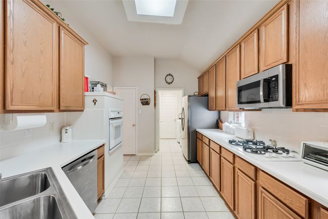 Kitchen featuring appliances with stainless steel finishes, vaulted ceiling, decorative backsplash, light tile patterned floors, and light countertops | Image 16