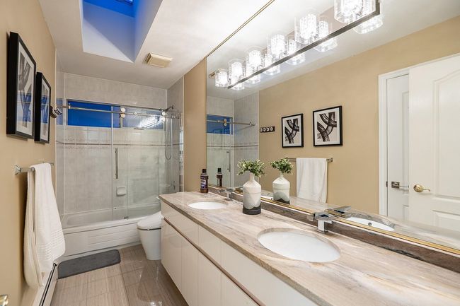 Bathroom featuring baseboard heating, combined bath / shower with glass door, double vanity, and toilet | Image 23