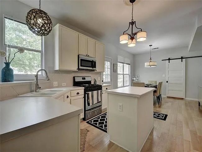 Kitchen featuring stainless steel appliances, a chandelier, a barn door, and light wood-style flooring | Image 11