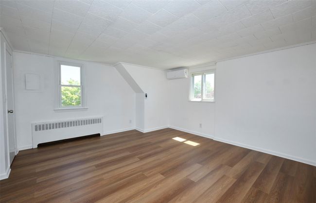 Bedroom featuring radiator heating unit, a wall unit AC, wood finished floors, and baseboards | Image 22
