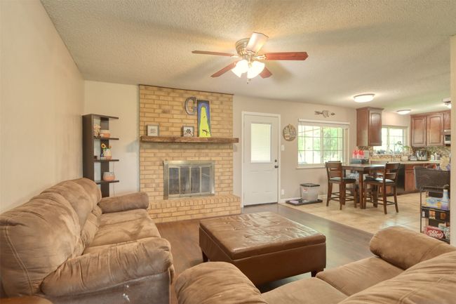 Living room with a ceiling fan, a textured ceiling, light wood-style floors, and a fireplace | Image 11