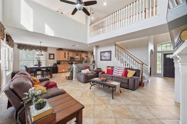 This spacious living area features high ceilings, a mix of tile and wood flooring, and an open concept connecting the kitchen and dining area. Large windows provide natural light, and there’s a stylish staircase leading to the second floor, enhancing the room's airy and inviting feel. | Image 16