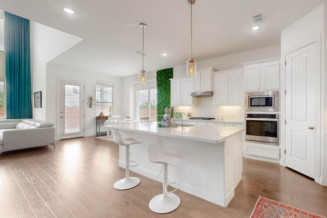 Kitchen with tasteful backsplash, light countertops, under cabinet range hood, stainless steel appliances, and wood finished floors | Image 10