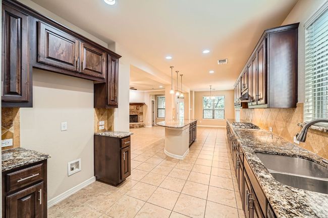 Kitchen featuring recessed lighting, dark brown cabinets, tasteful backsplash, light stone counters, and decorative light fixtures | Image 12