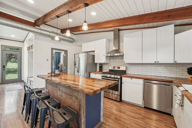 Kitchen with wood counters, wall chimney range hood, stainless steel appliances, backsplash, and white cabinetry | Image 11