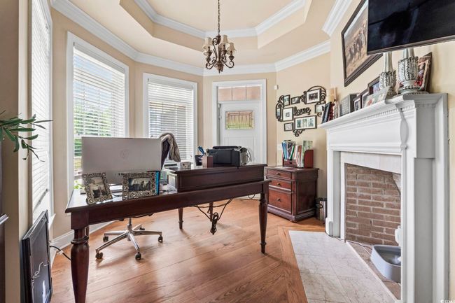 Office area with a chandelier, a tray ceiling, light wood-style floors, ornamental molding, and a fireplace with flush hearth | Image 14