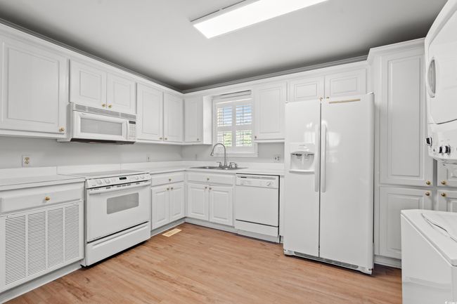 Kitchen featuring white appliances, stacked washing machine and dryer, and light countertops | Image 35