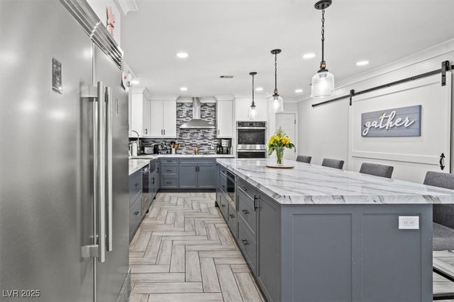 Kitchen featuring stainless steel appliances, gray cabinetry, decorative backsplash, a barn door, and wall chimney range hood | Image 5