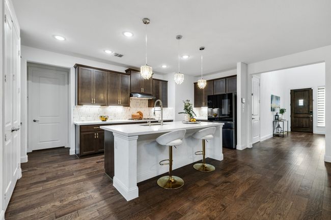 Kitchen with black fridge, decorative light fixtures, dark brown cabinets, dark hardwood / wood-style floors, and a kitchen island with sink | Image 9