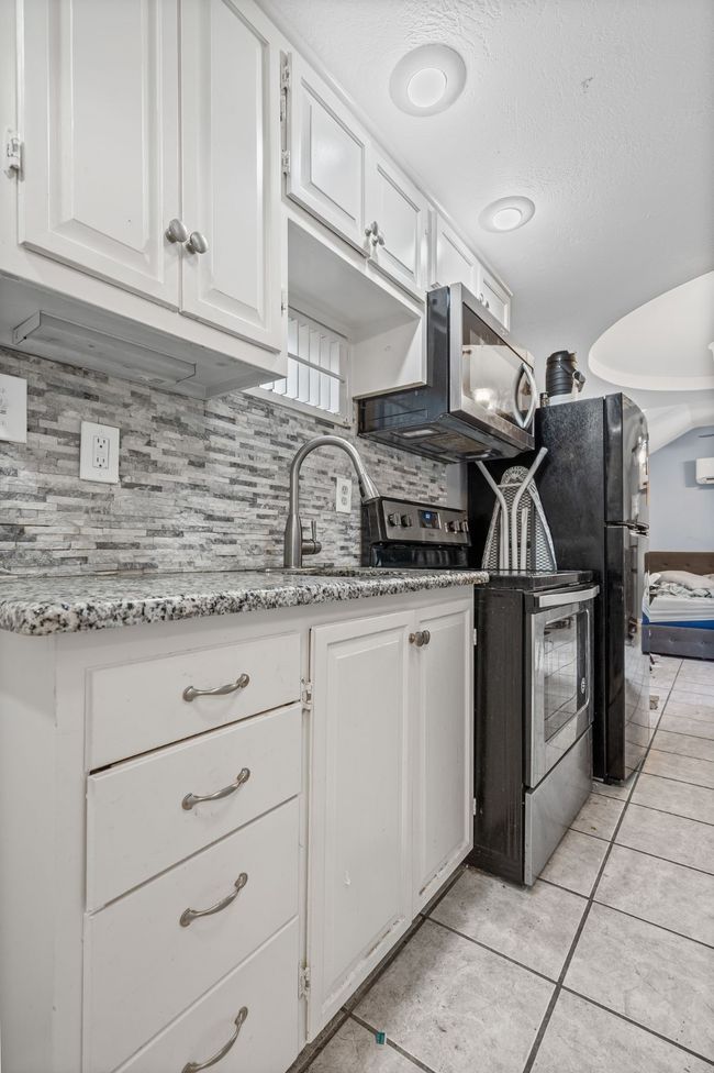Kitchen with stainless steel appliances, white cabinetry, backsplash, light tile patterned flooring, and light stone countertops | Image 22