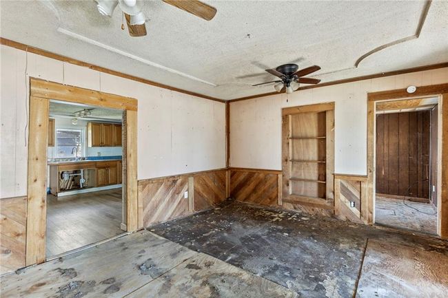 Spare room featuring a ceiling fan, wooden walls, a textured ceiling, and wood finished floors | Image 6