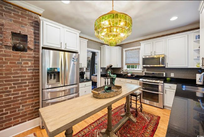 Kitchen featuring appliances with stainless steel finishes, dark countertops, white cabinetry, open shelves, and decorative light fixtures | Image 27